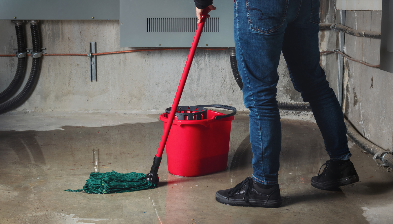 Person mopping floodwater from leaks in basement or electrical room.