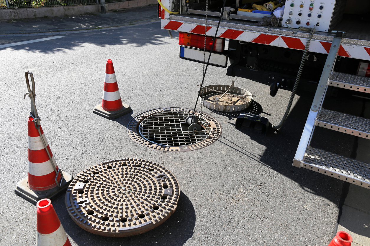 Sewer camera inspection on a street with orange cones around the work area and manhole covers.